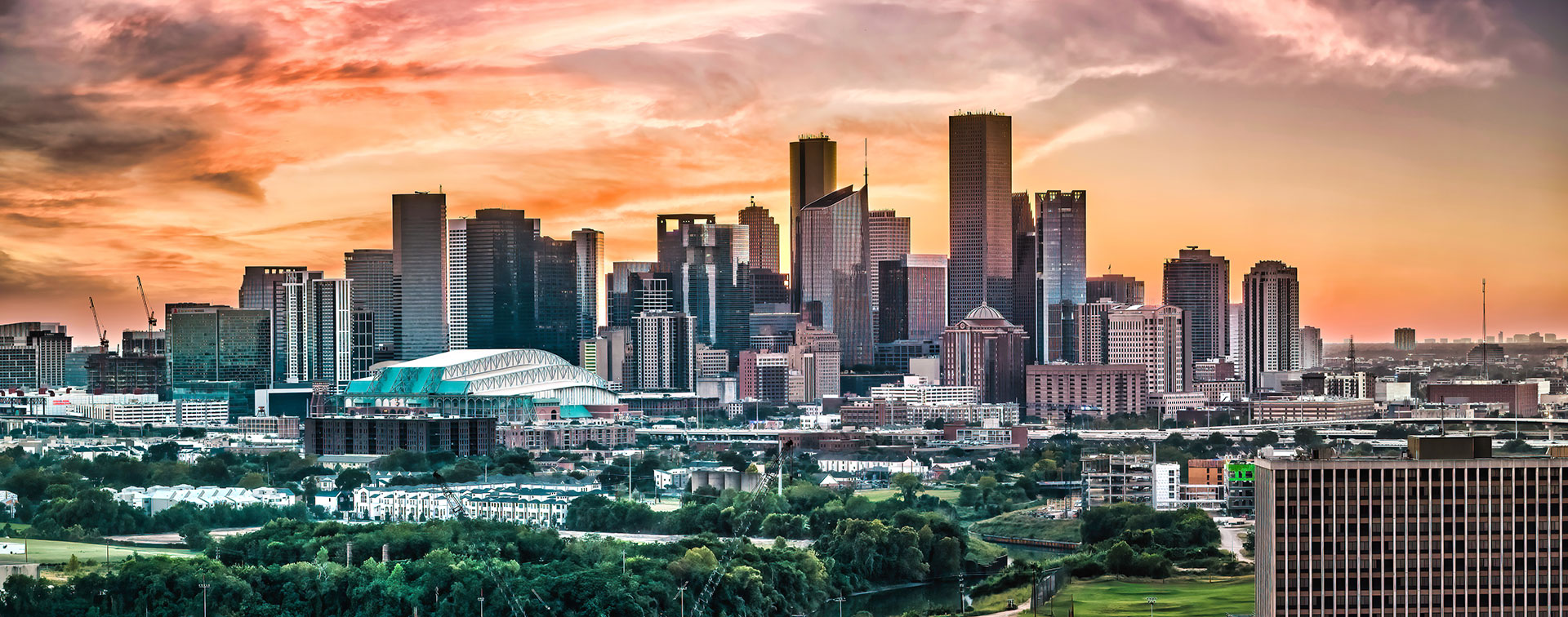 The image depicts a city skyline at sunset with a panoramic view of downtown buildings and a clear sky, taken from an elevated perspective.