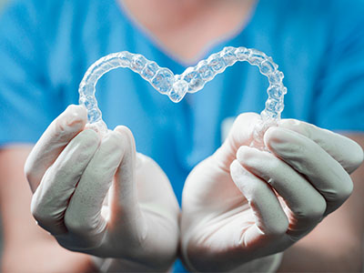 A person wearing white gloves holds a transparent heart-shaped object with dental implants inside, symbolizing love for dental health.