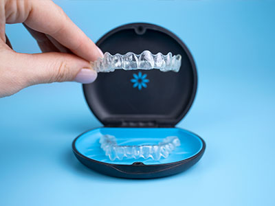A hand holding a clear plastic tray with a blue mouthguard inside, shown against a light blue background.