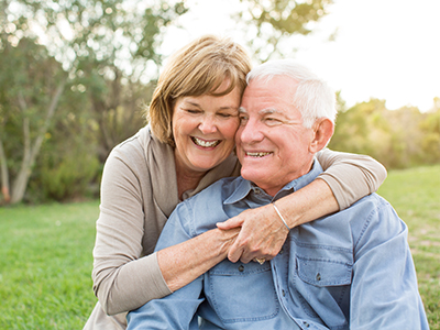 The image shows an elderly couple embracing each other outdoors during daytime.