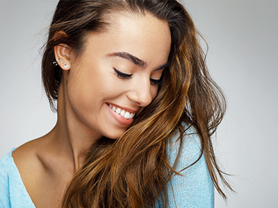 A smiling woman with long hair and earrings, looking away from the camera, against a white background.