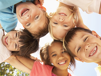 The image shows a group of six children with diverse expressions, posing for a photo outdoors with clear skies, smiling at the camera.