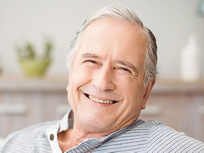 The image shows an elderly man sitting comfortably with his head turned towards the camera, smiling broadly, and looking relaxed.